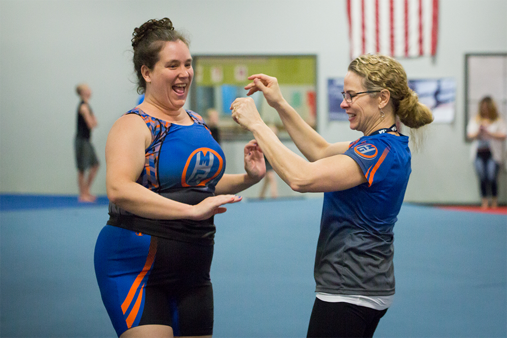 Athlete Tiffany and her coach Michaela. both wearing team uniforms, celebrate at a gymnastics competition