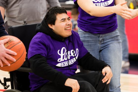 A student wearing a purple "Live Unified" shirt smiles at the Live Unified event at Target Center,